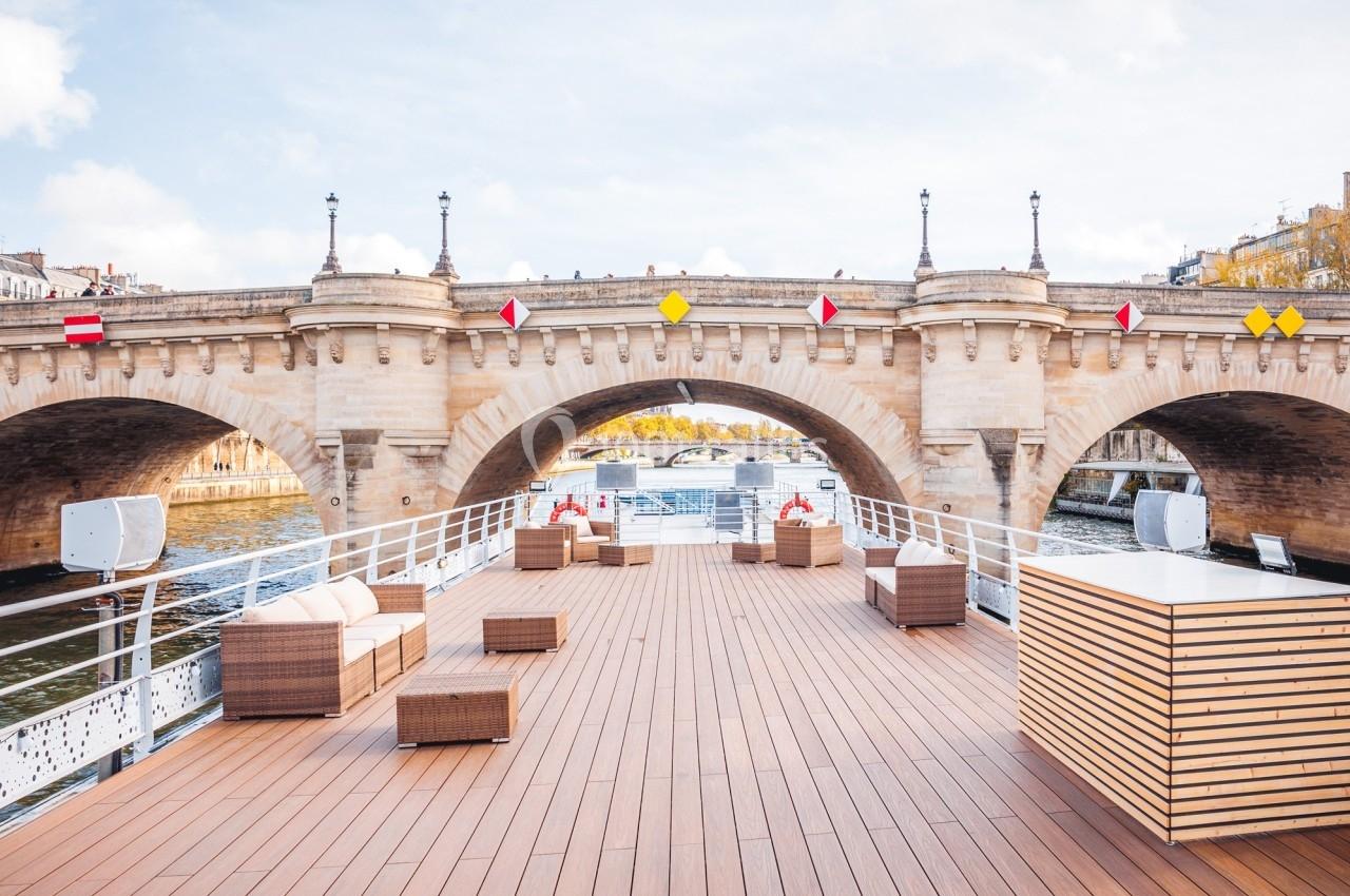Pont en pierre traversant une rivière, vu depuis le ponton d'un bateau aménagé avec des meubles en rotin.