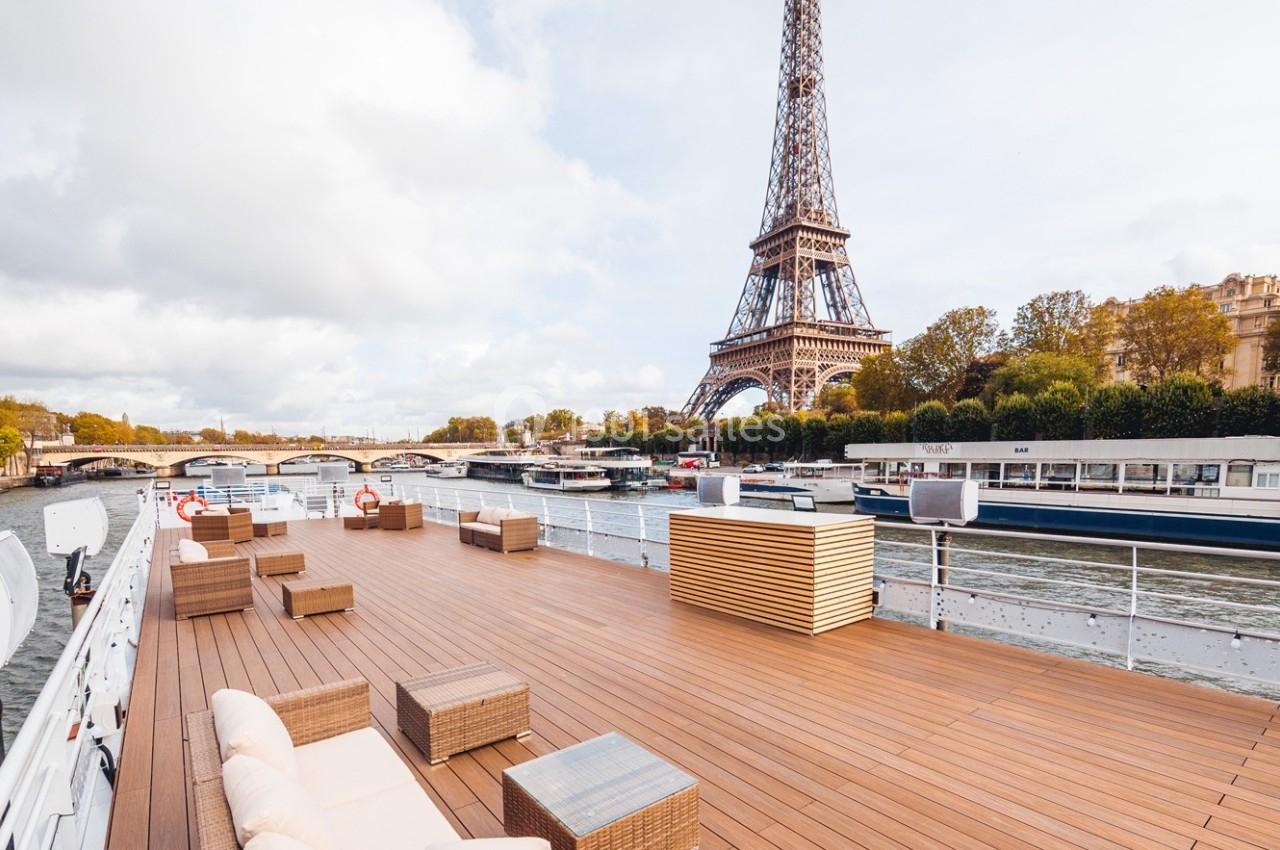 Terrasse en bois d'un bateau sur la Seine avec vue sur la tour Eiffel et les quais parisiens.