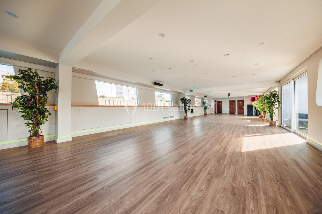 Salle spacieuse avec parquet clair, grandes fenêtres laissant entrer la lumière naturelle et plantes en pot.