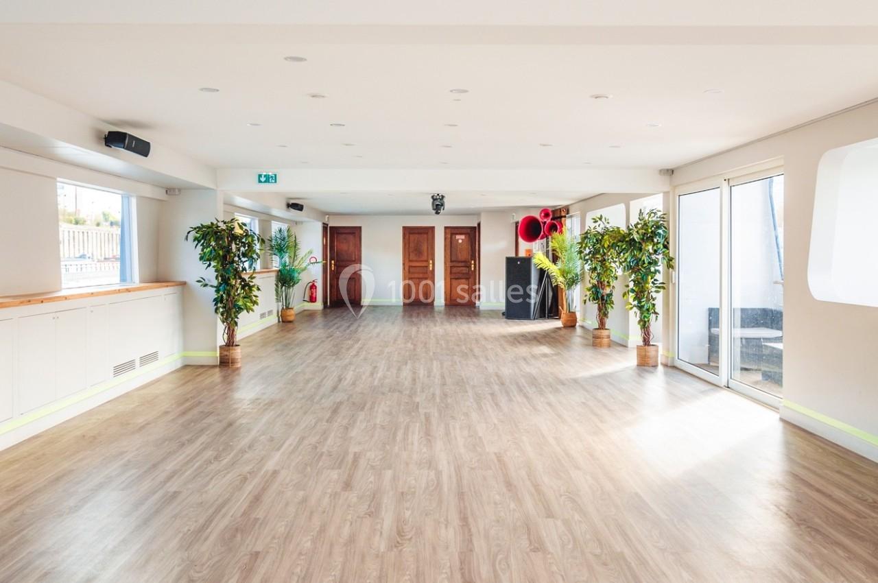 Salle lumineuse avec parquet, plantes en pot, grandes portes en bois et baies vitrées donnant sur l'extérieur.