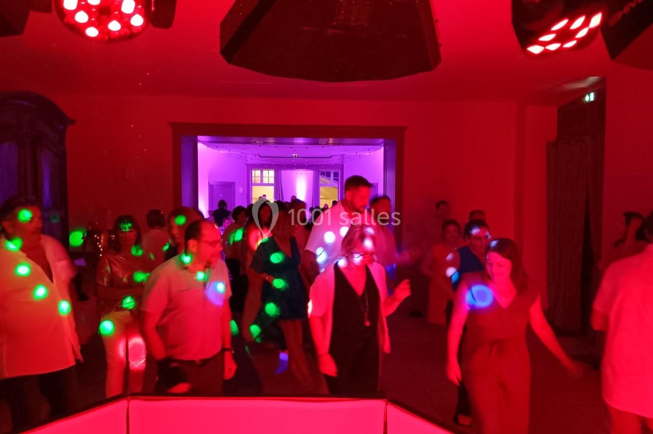 Des personnes dansent dans une salle éclairée par des lumières rouges et vertes lors d'un événement festif.
