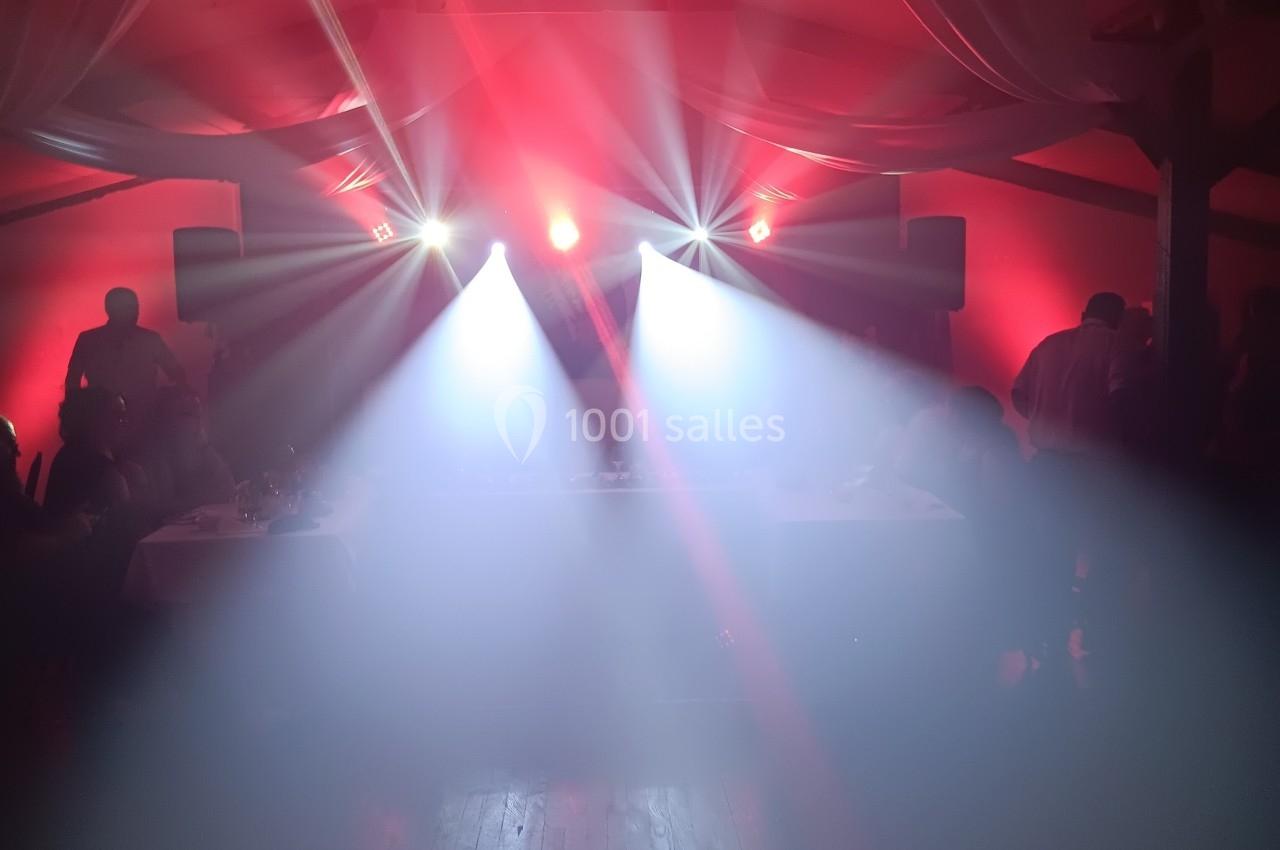 Salle plongée dans une ambiance festive avec éclairage rouge et projecteurs lumineux diffusant de la fumée.