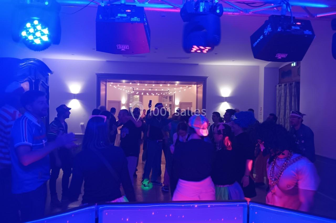 Personnes dansant dans une salle éclairée par des lumières colorées, ambiance festive et décontractée.