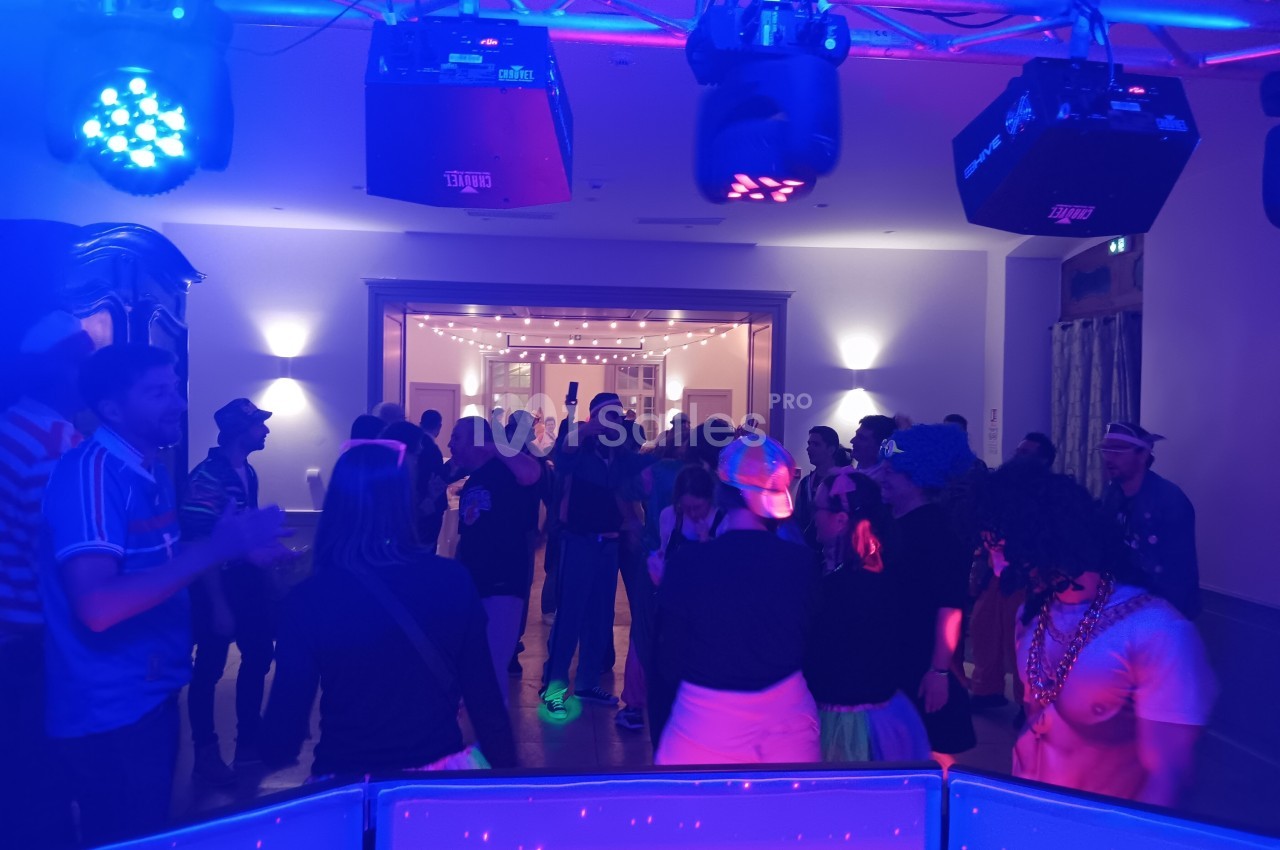 Personnes dansant dans une salle éclairée par des lumières colorées, ambiance festive et décontractée.