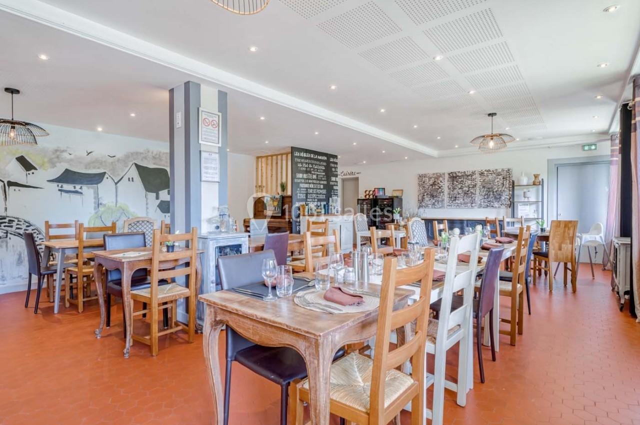 Salle de restaurant lumineuse avec tables en bois dressées, sol en terre cuite et décoration murale sobre.