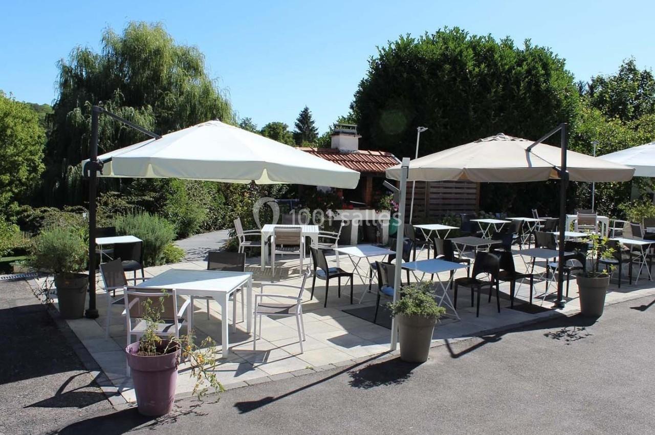 Terrasse extérieure avec tables et chaises sous des parasols, entourée de végétation et baignée de lumière.