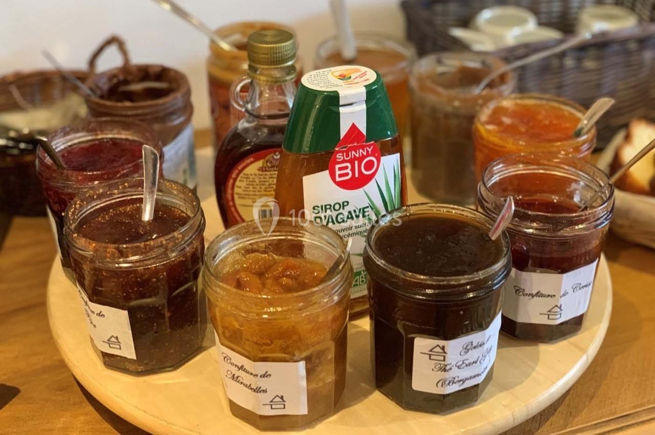 Plateau de pots de confitures variées, sirop d'agave et miel, disposés sur une table en bois.