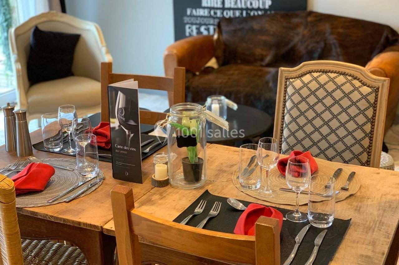Table dressée avec des verres, serviettes rouges et menu, entourée de chaises dans un intérieur chaleureux.