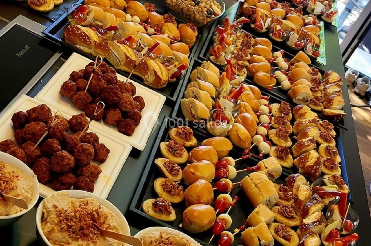 Buffet varié avec mini-sandwichs, brochettes, boulettes, salades et desserts disposés sur une grande table.