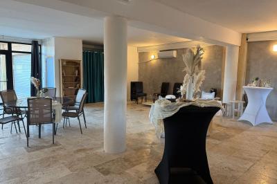 Salle lumineuse avec une grande table décorée de fleurs roses, entourée de chaises blanches, et un espace en arrière-plan.