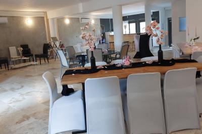 Salle lumineuse avec une grande table décorée de fleurs roses, entourée de chaises blanches, et un espace en arrière-plan.