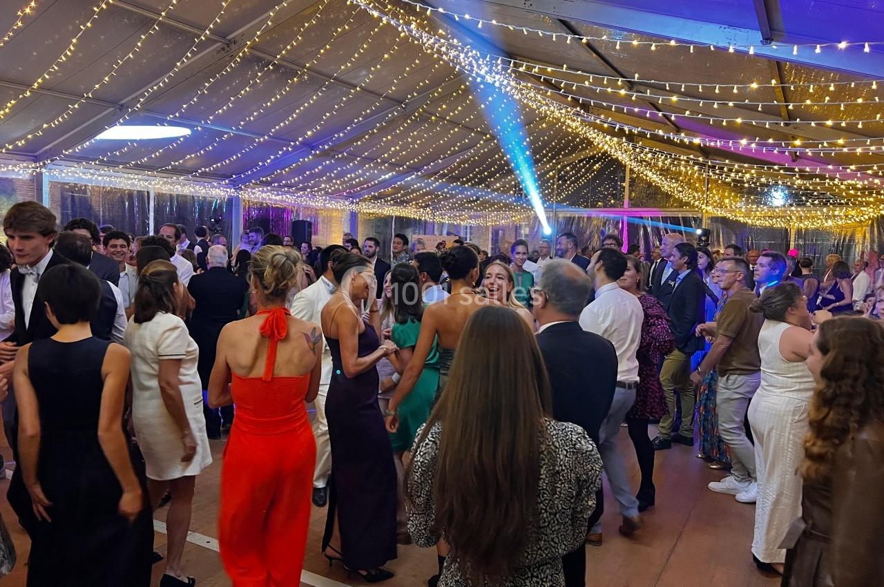 Des personnes dansent sous une tente éclairée par des guirlandes lumineuses lors d'un événement festif.