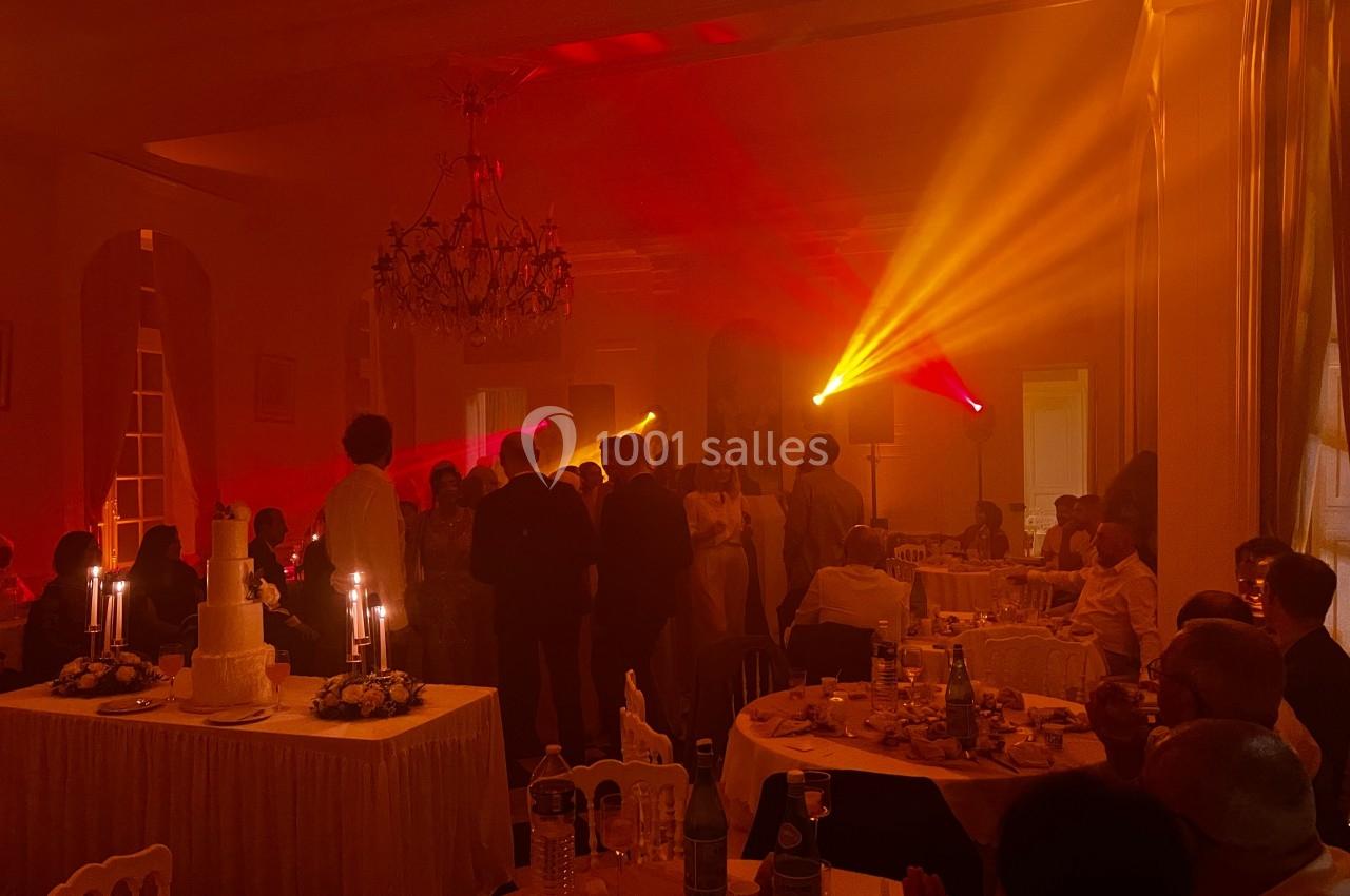 Salle de réception éclairée par des lumières colorées, avec des invités rassemblés et des tables dressées.