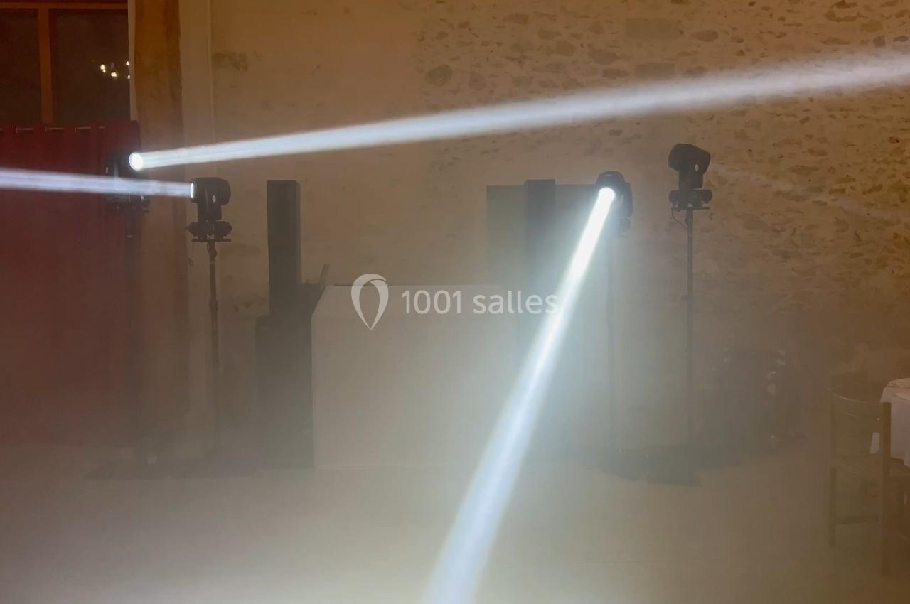 Deux faisceaux lumineux blancs traversent une salle sombre avec des murs en pierre apparente.