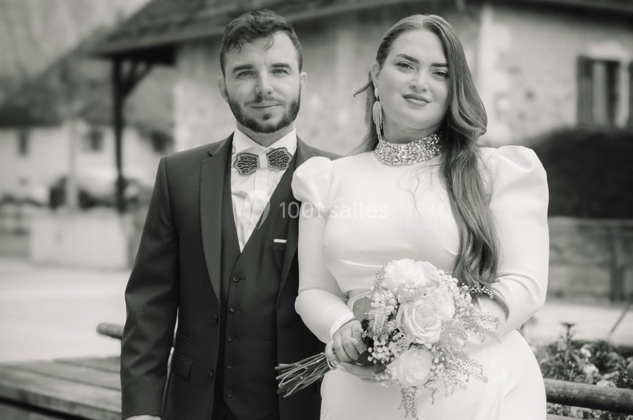 Un couple en tenue de mariage pose ensemble devant un bâtiment en arrière-plan flou.