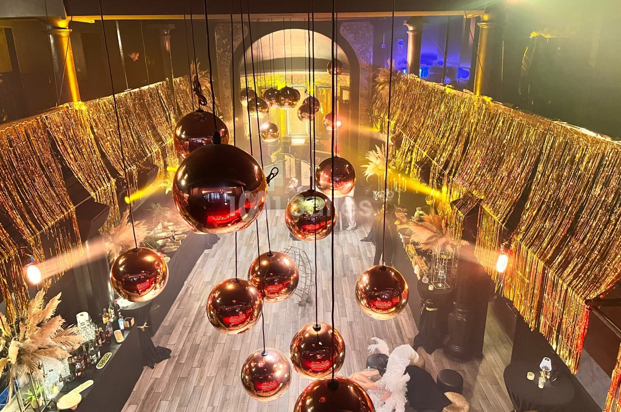 Suspension de boules rouges brillantes dans une salle décorée de guirlandes dorées et éclairée par des lumières chaudes.