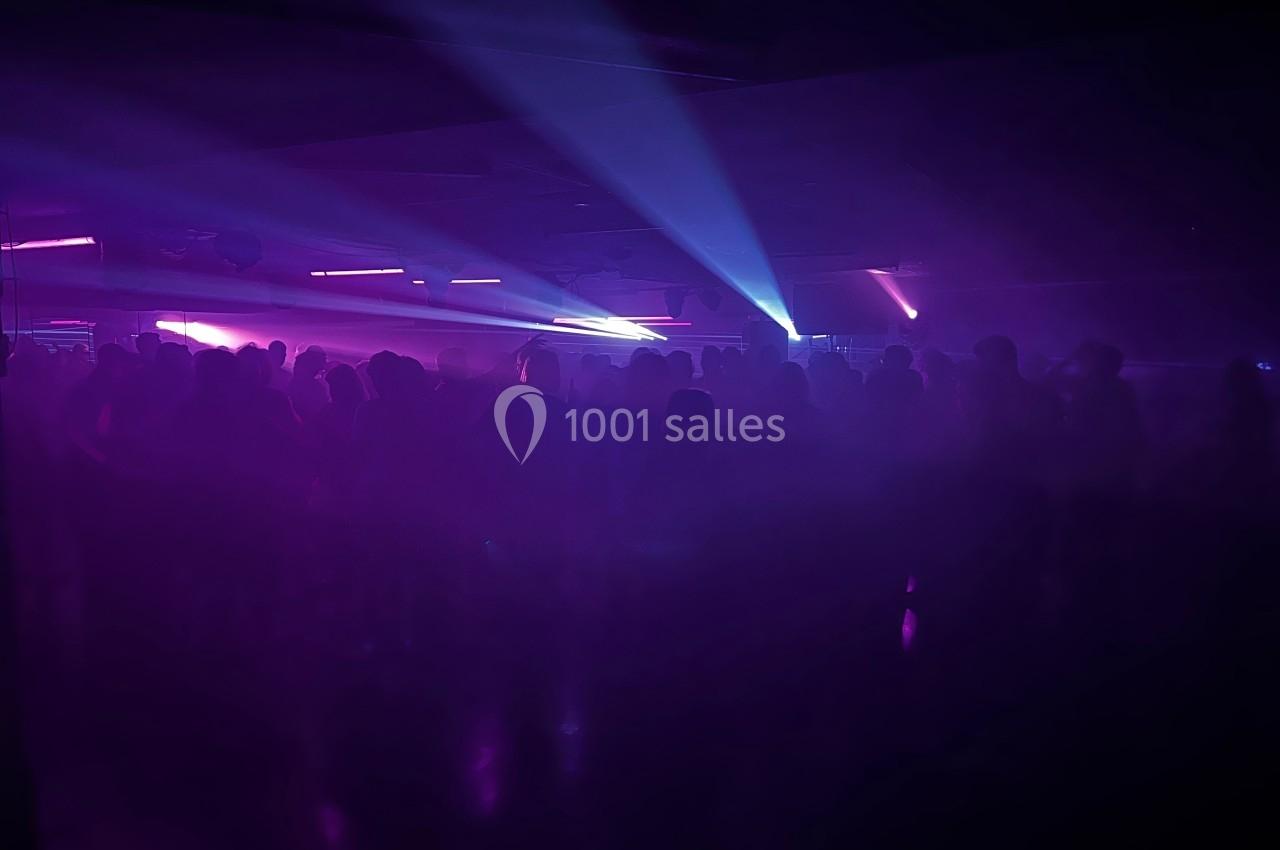 Foule dans une salle sombre éclairée par des lumières violettes et bleues, créant une ambiance festive.