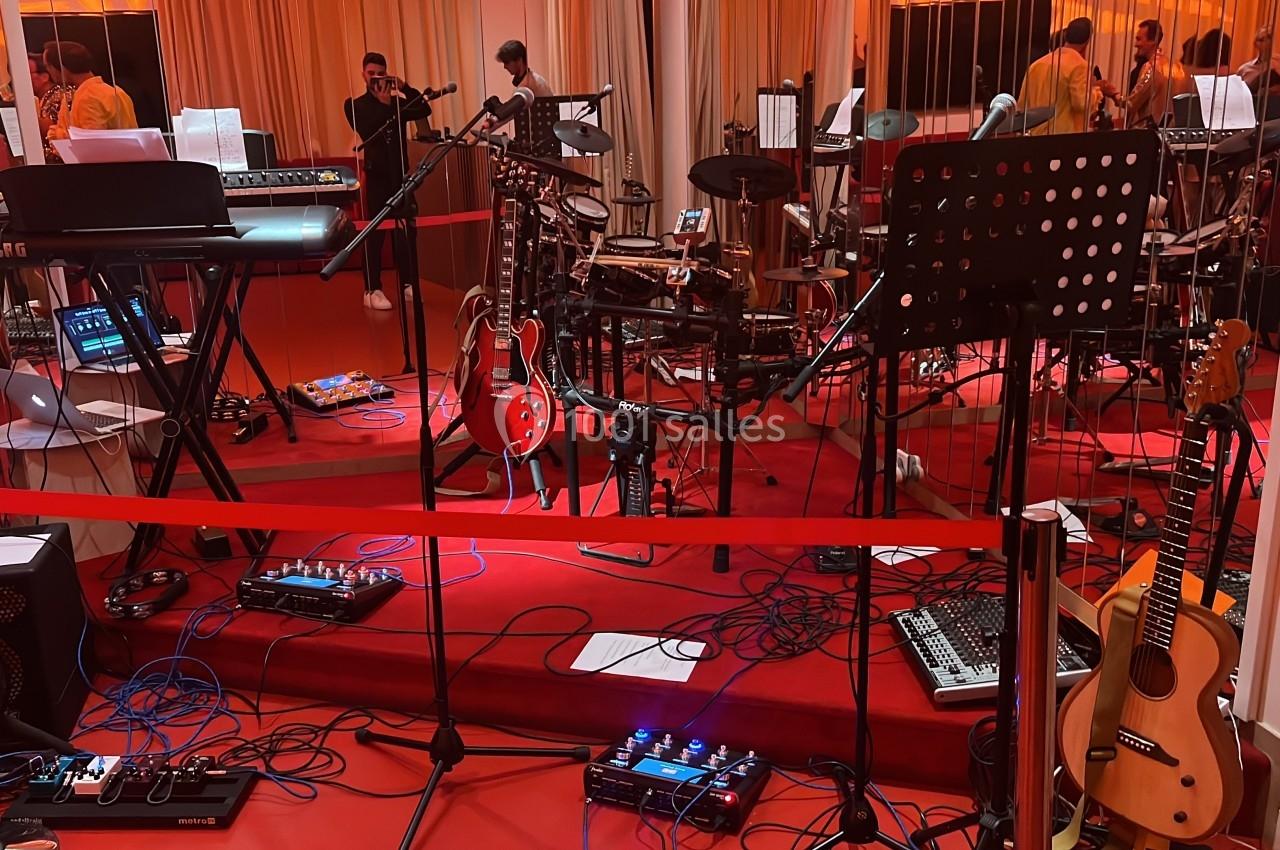 Salle de répétition avec instruments de musique variés, dont claviers, guitares, batterie et matériel audio.