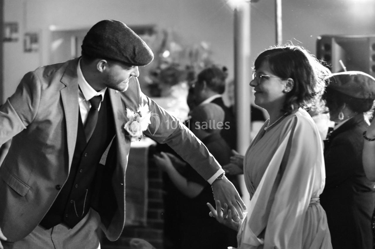Un homme en costume et une femme en robe échangent un geste complice lors d'un événement festif.
