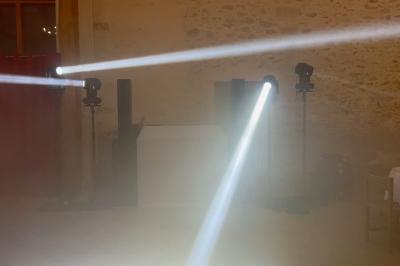 Deux faisceaux lumineux blancs traversent une salle avec des murs en pierre, éclairant un espace légèrement enfumé.