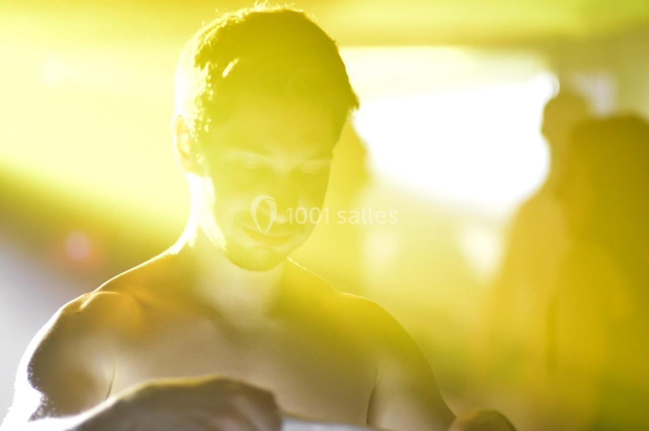 Un homme torse nu dans une lumière jaune intense, entouré de silhouettes floues en arrière-plan.