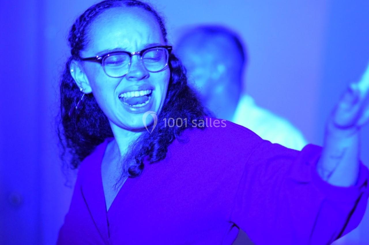 Femme portant des lunettes chantant ou s'exprimant avec émotion sous un éclairage bleu vif.