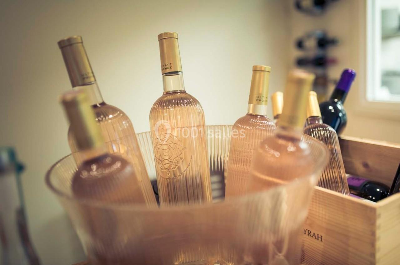 Bouteilles de vin rosé dans un seau transparent, avec des bouteilles de vin rouge en arrière-plan.