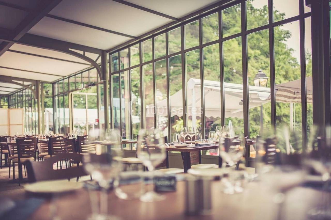 Salle de restaurant lumineuse avec de grandes baies vitrées donnant sur un espace extérieur verdoyant.