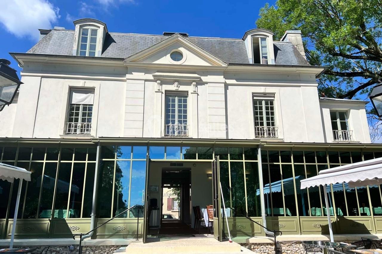 Façade d'un bâtiment élégant avec grandes fenêtres, entouré de terrasses et d'arbres sous un ciel bleu.