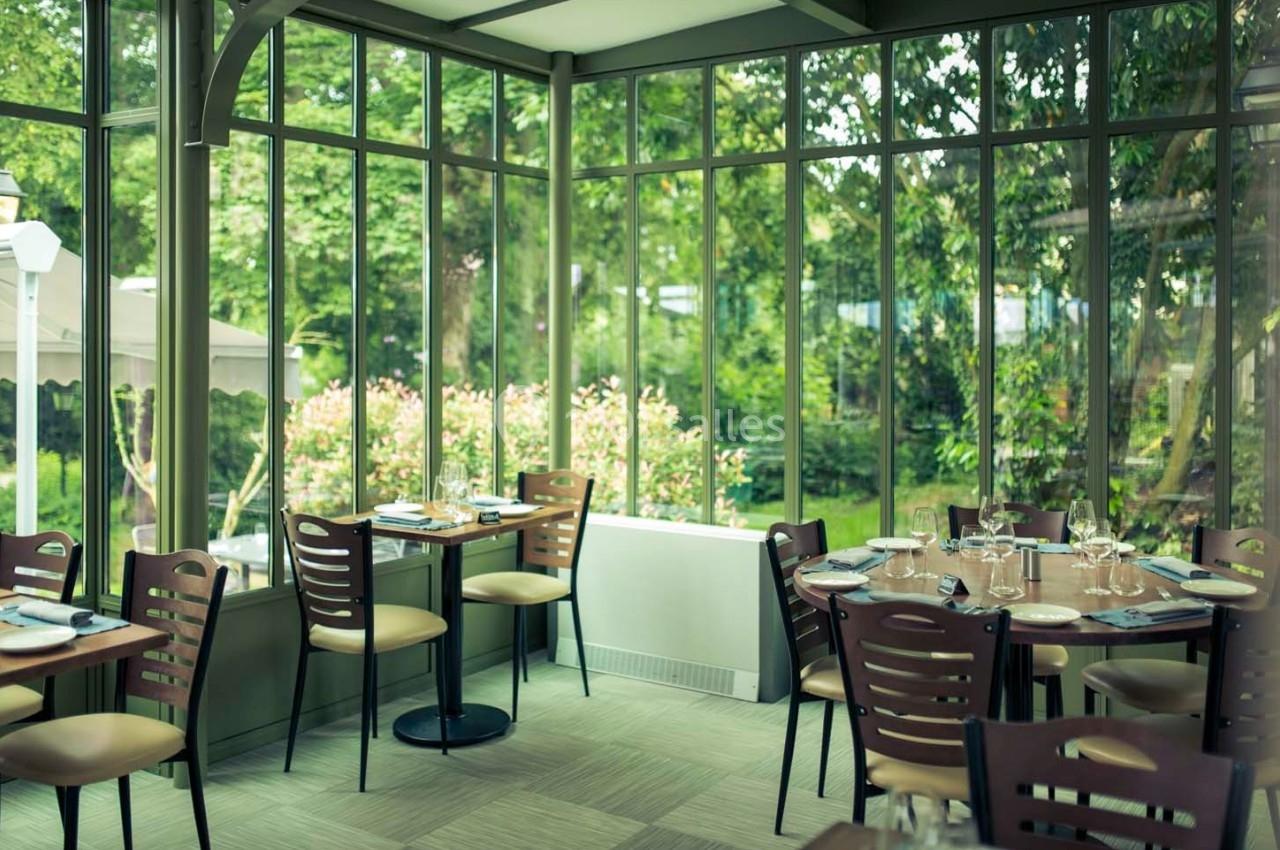 Salle de restaurant lumineuse avec de grandes baies vitrées donnant sur un jardin verdoyant.