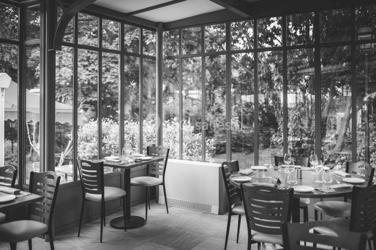 Salle de restaurant lumineuse avec de grandes baies vitrées donnant sur un jardin arboré.