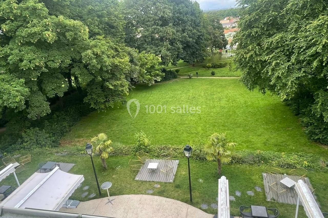 Vue d'un jardin verdoyant avec pelouse, arbres et terrasses aménagées, prise depuis une hauteur.