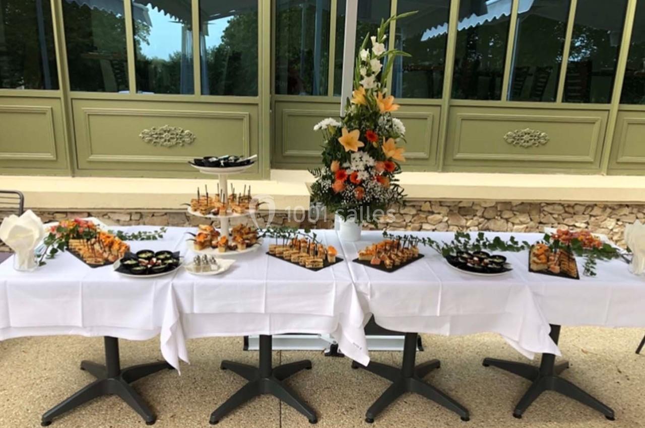 Buffet dressé en extérieur avec divers plats et amuse-bouches sur des plateaux, décoré de fleurs et verdure.