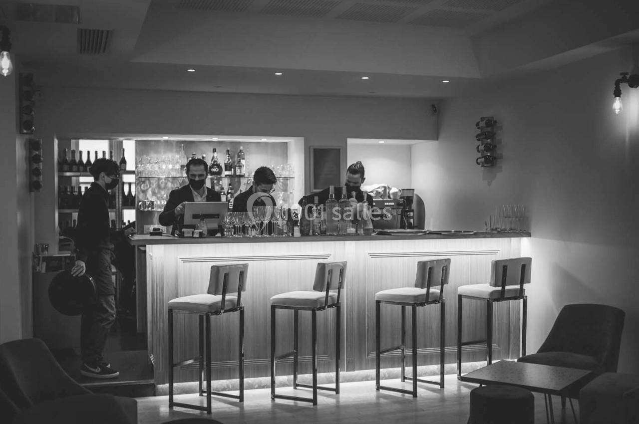 Bar moderne en noir et blanc avec quatre tabourets alignés et des serveurs derrière le comptoir éclairé.