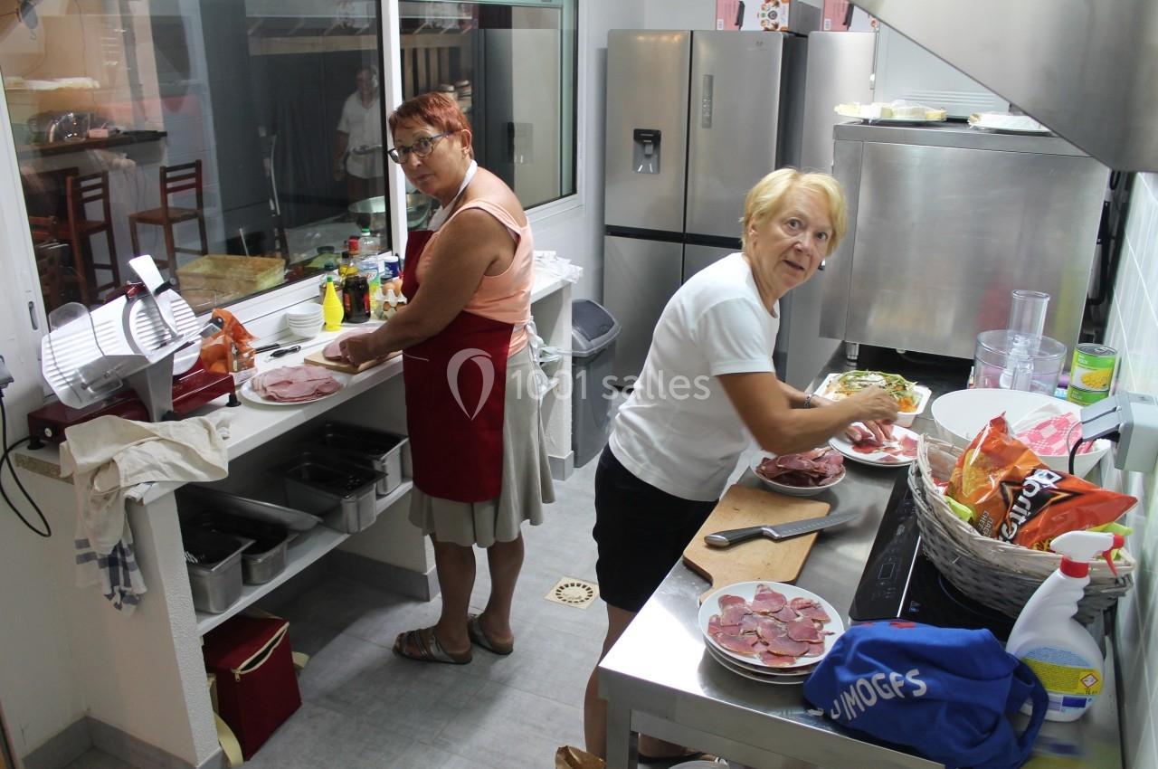 Deux femmes préparent des assiettes de charcuterie dans une cuisine professionnelle.