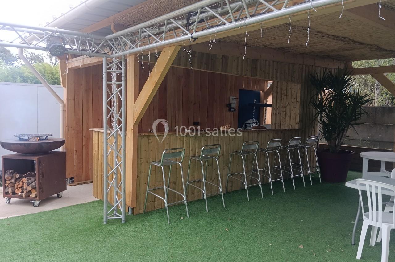 Bar extérieur en bois avec tabourets hauts, plan de travail, barbecue à gauche et plantes en pot sur sol en gazon…