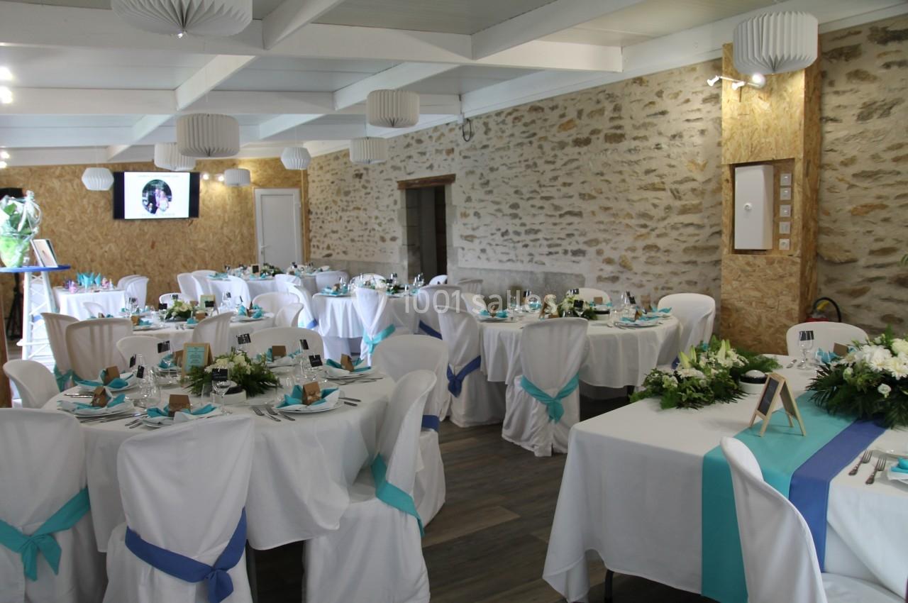 Salle de réception décorée avec des tables rondes, nappes blanches, rubans turquoise et arrangements floraux.