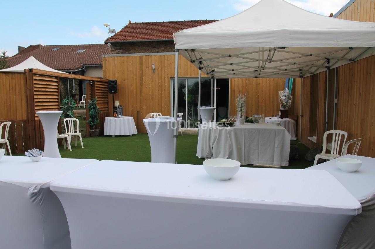 Espace extérieur aménagé avec tentes blanches, tables nappées et chaises, entouré de clôtures en bois.
