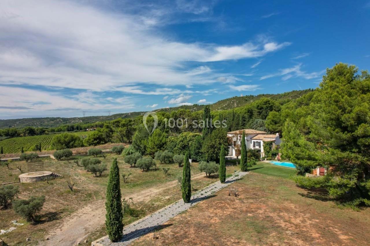 Vue aérienne d'une maison entourée de cyprès, d'oliviers et de végétation, avec une piscine et des collines en arrière-plan.