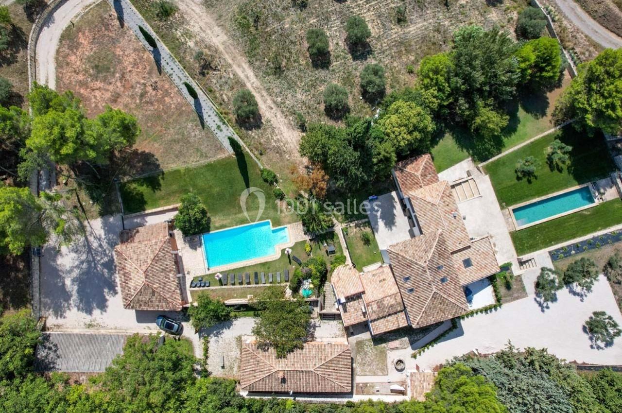 Vue aérienne d'une propriété avec plusieurs bâtiments, une piscine, des jardins et des espaces verts environnants.