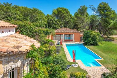 Salon avec canapé beige, fauteuils, table basse, télévision, cheminée en pierre et plafond avec poutres apparentes.