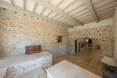 Salon avec canapé beige, fauteuils, table basse, télévision, cheminée en pierre et plafond avec poutres apparentes.