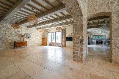 Salon avec canapé beige, fauteuils, table basse, télévision, cheminée en pierre et plafond avec poutres apparentes.