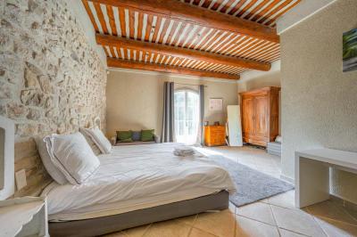 Salon avec canapé beige, fauteuils, table basse, télévision, cheminée en pierre et plafond avec poutres apparentes.