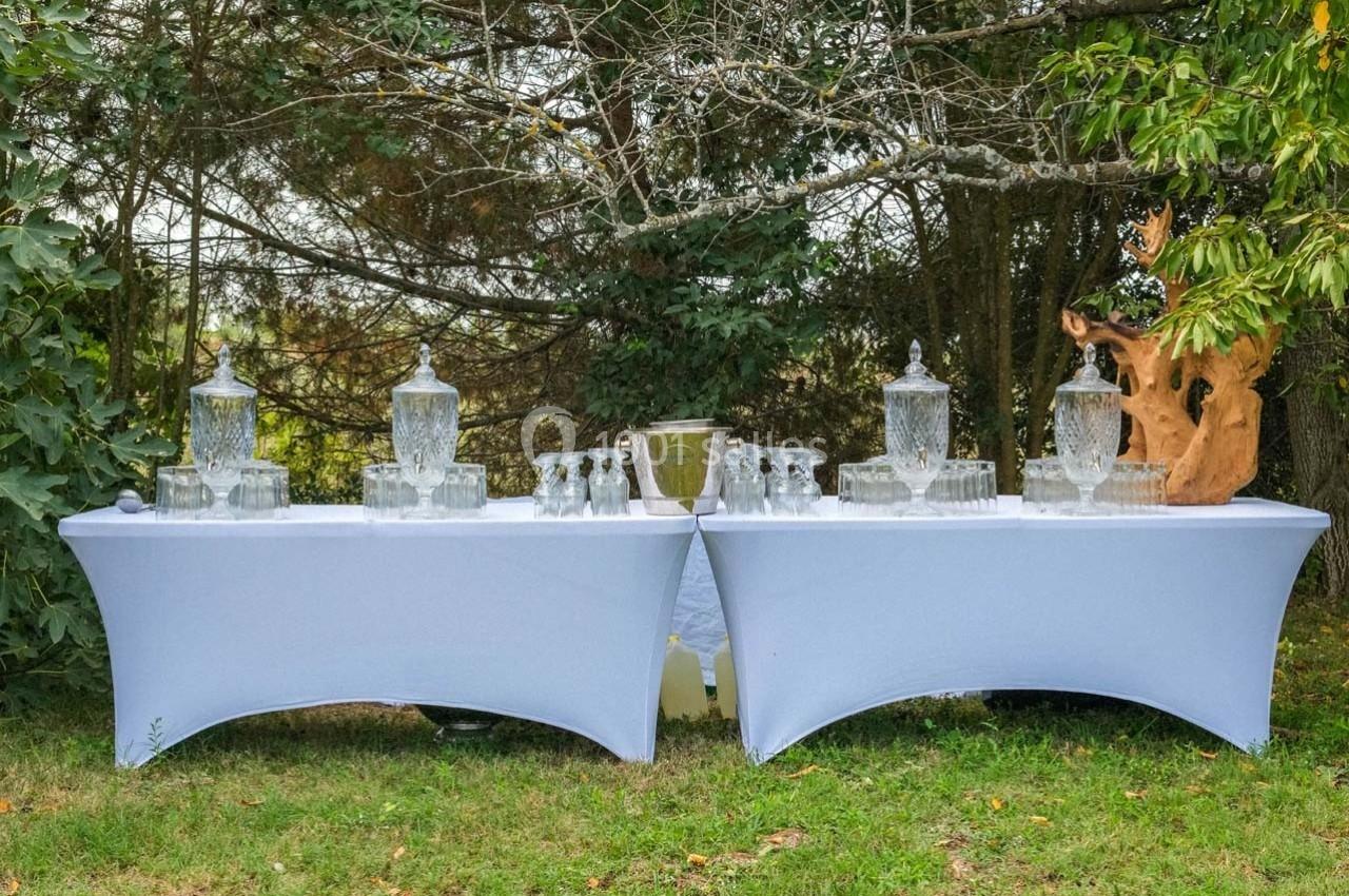 Deux tables recouvertes de nappes blanches avec des fontaines à boissons, verres et décorations en extérieur.