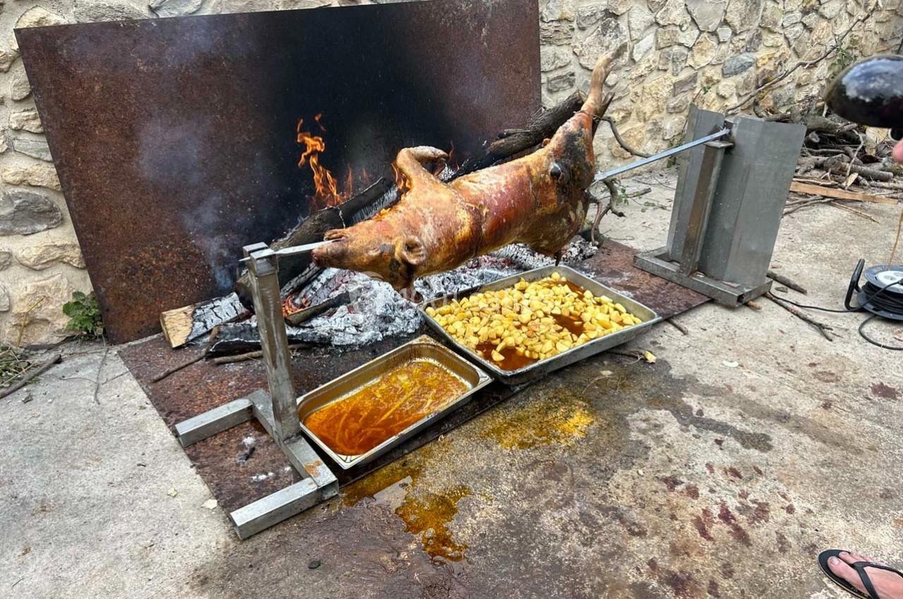 Cochon rôti à la broche au-dessus de braises, accompagné de pommes de terre et de sauce dans des plats en métal.