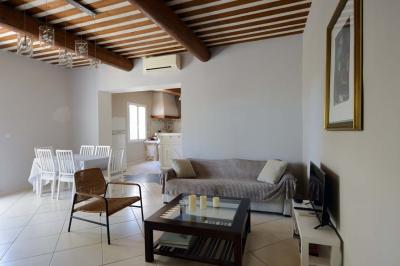 Salon avec canapé beige, fauteuils, table basse, télévision, cheminée en pierre et plafond avec poutres apparentes.