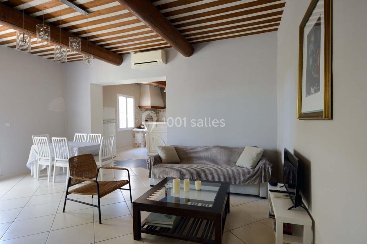 Salon lumineux avec canapé, table basse, chaise en osier, table à manger et cuisine ouverte en arrière-plan.