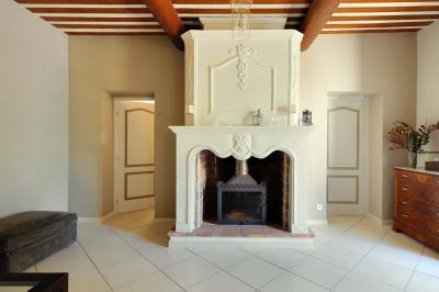 Salon avec canapé beige, fauteuils, table basse, télévision, cheminée en pierre et plafond avec poutres apparentes.