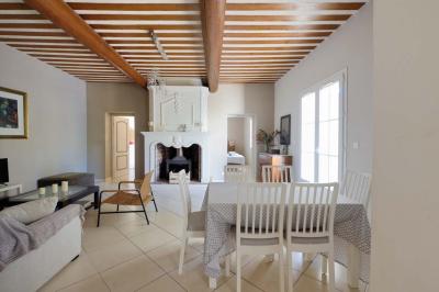 Salon avec canapé beige, fauteuils, table basse, télévision, cheminée en pierre et plafond avec poutres apparentes.